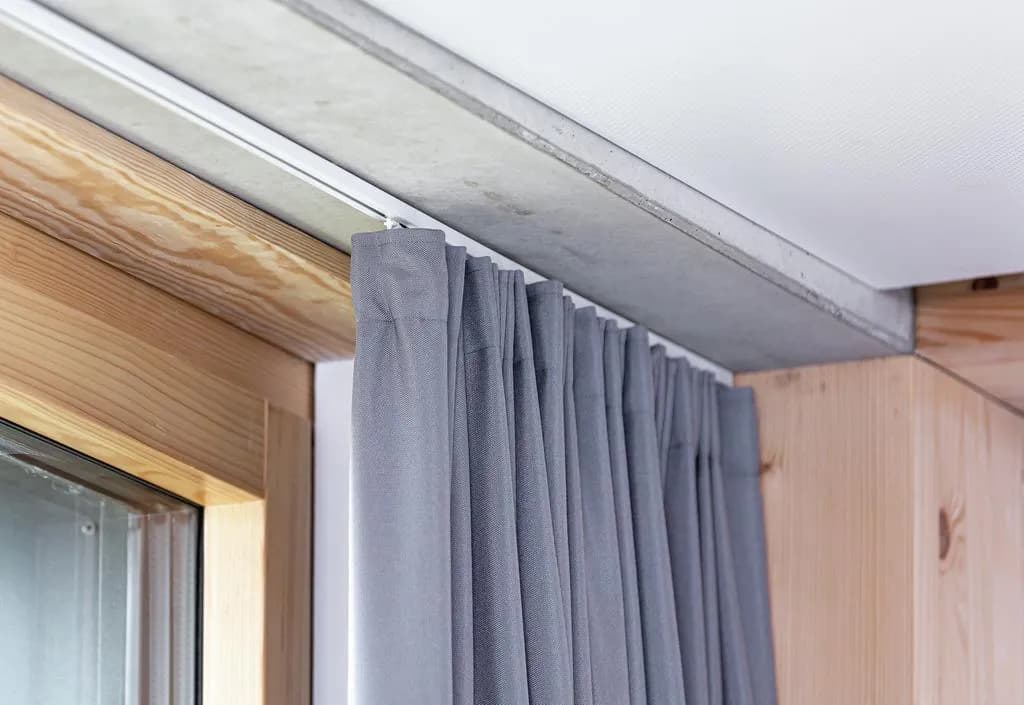 Ceiling-mounted curtain track positioned near a concrete window beam in an apartment.